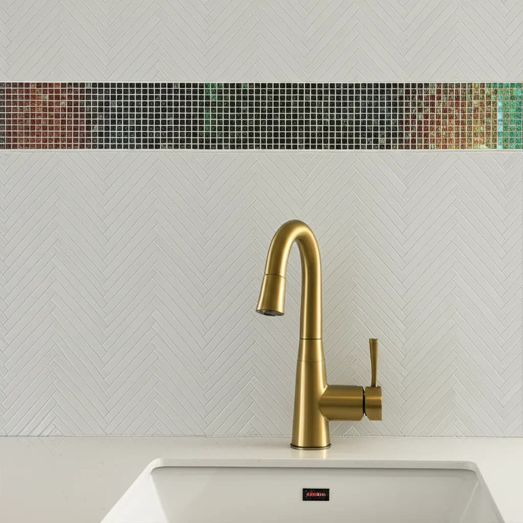 Close view of a brushed-gold faucet over an undermount sink against white herringbone tile with an iridescent glass mosaic band