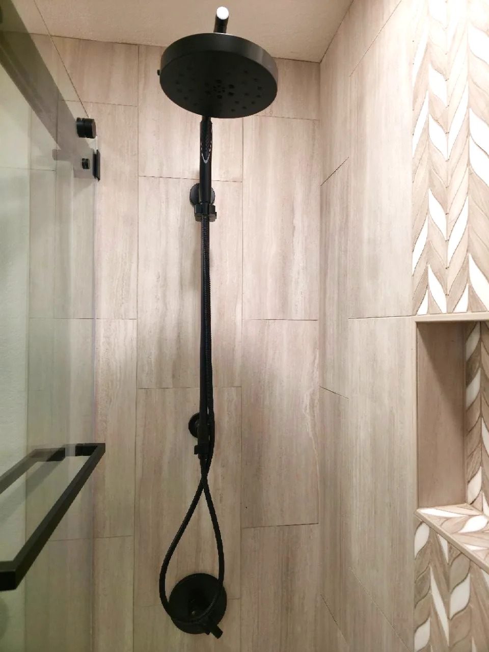 After: matte black rain head and handheld beside the chevron mosaic accent and niche