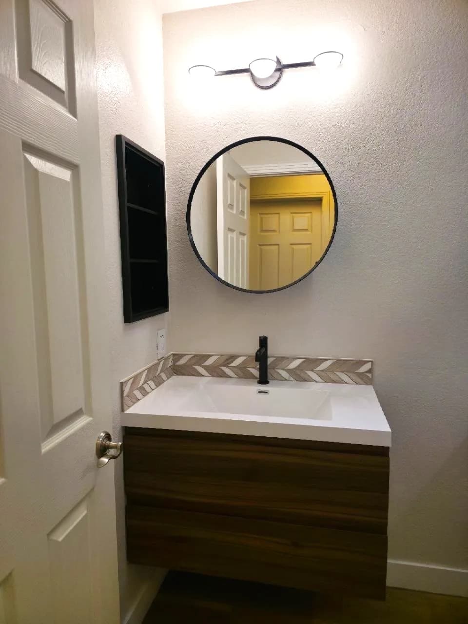 After: floating walnut vanity with black faucet, round mirror and three-globe light