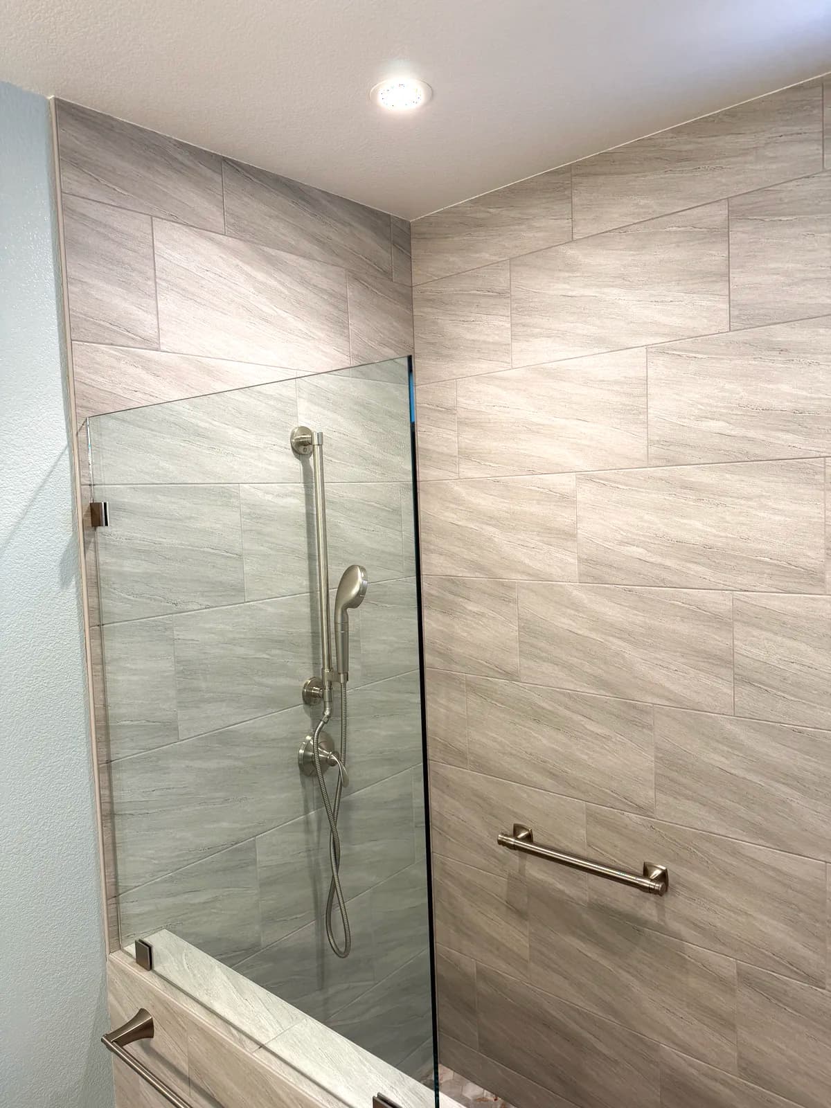 After: frameless glass panel and grey porcelain shower with recessed ceiling lights