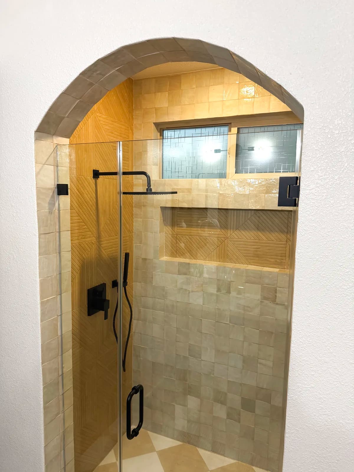 After: arched shower entry with frameless glass panel and glossy cream tile