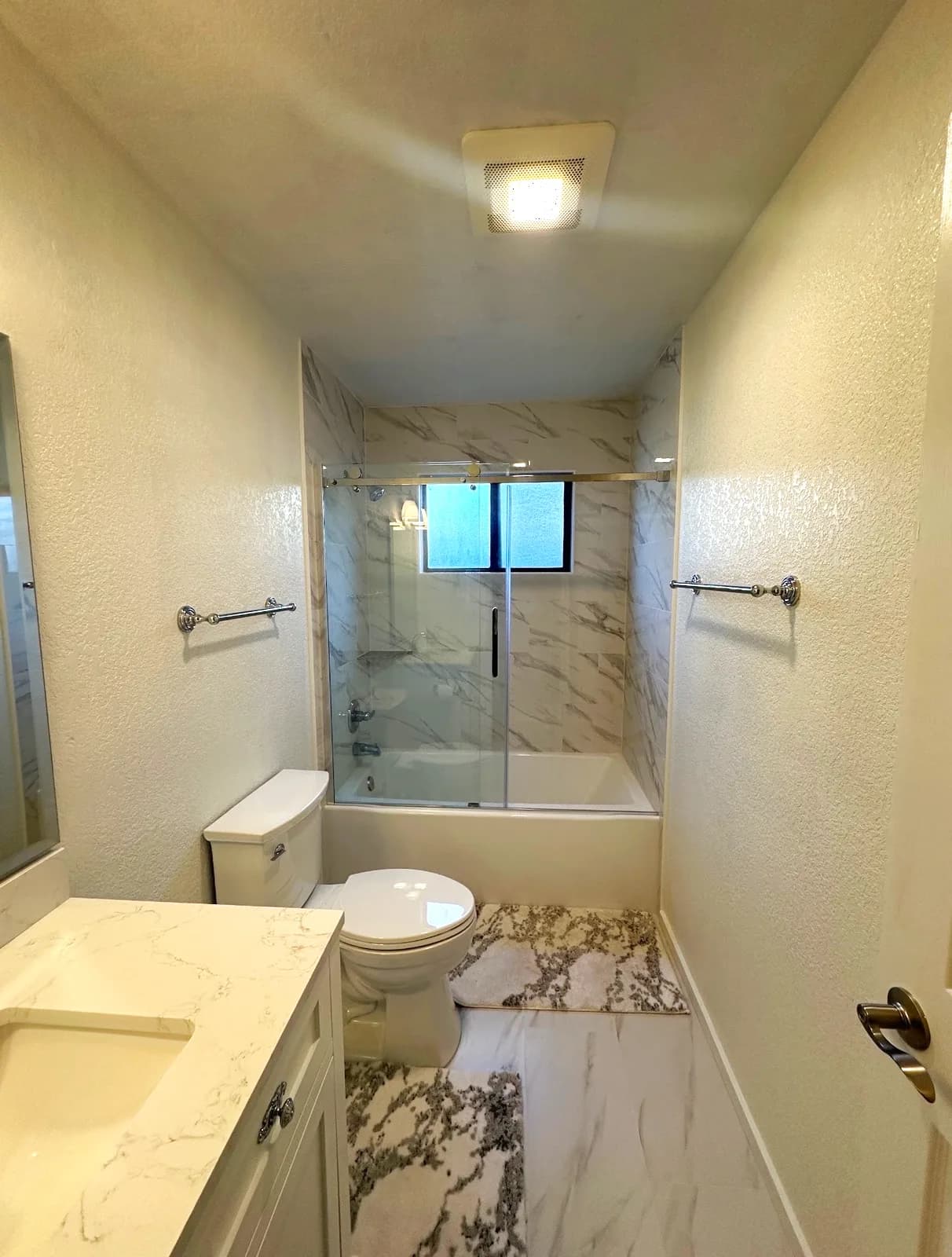 After: Folsom hall bathroom with marble-look tub surround, frameless sliding door, white vanity and marble-look floor