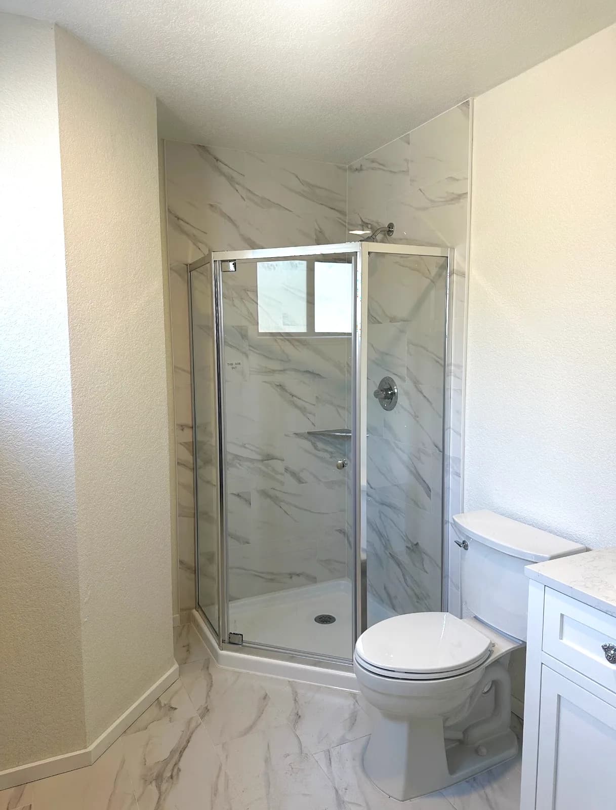 After: neo-angle shower in marble-look porcelain with glass enclosure and new white vanity