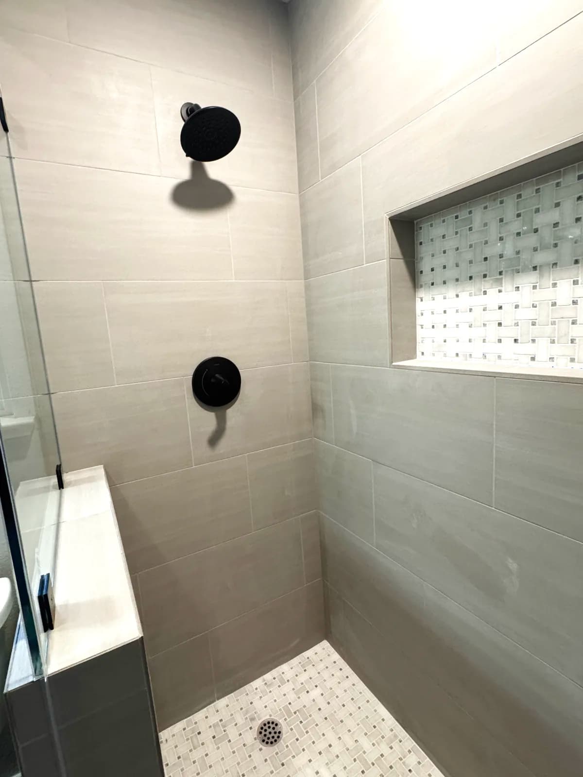 After: matte black rain head and handheld beside the mosaic-lined niche