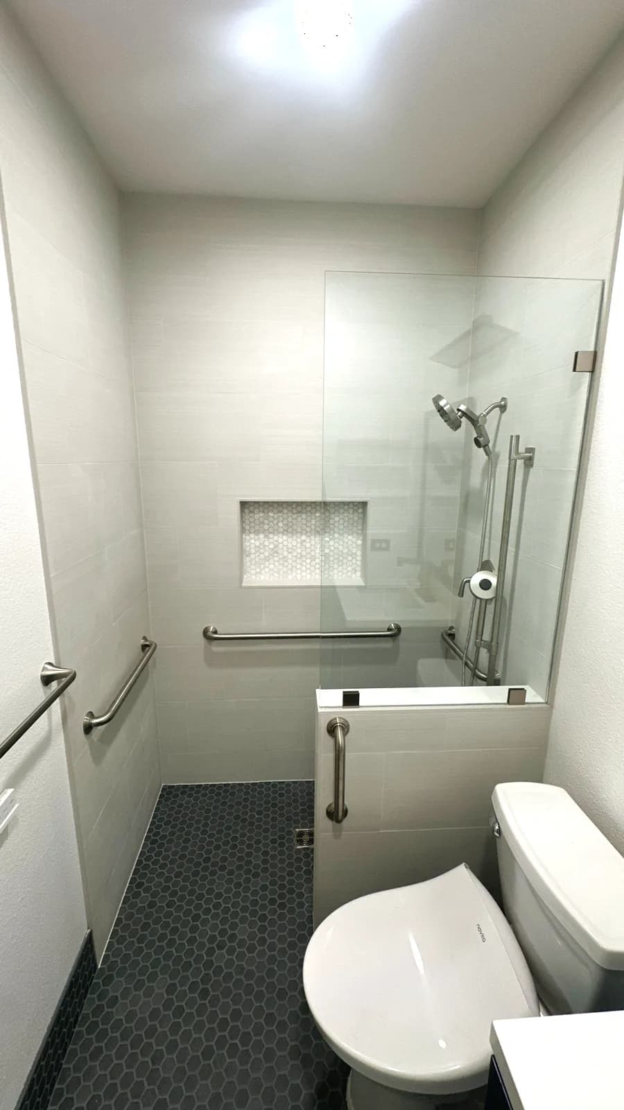 After: low-threshold shower with white tile, niche, black pebble floor, grab bars and glass panel in Roseville, CA