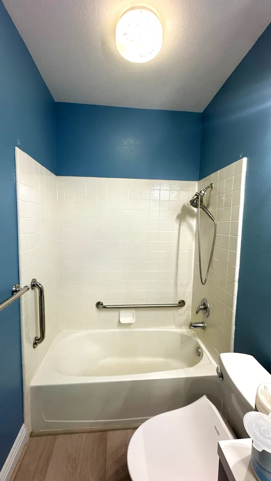 Before: Roseville bathroom with tub, clip-on grab bars and dark blue walls