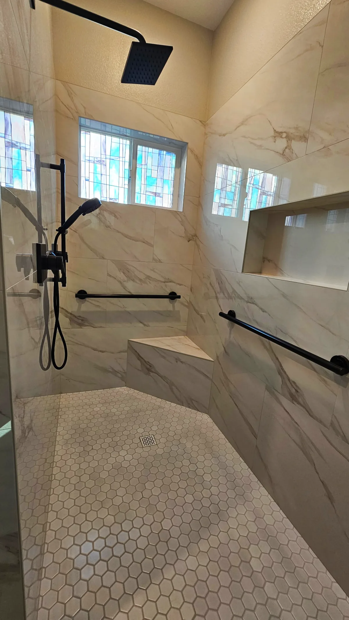 After: Roseville roll-in shower full depth with matte black square rain head, handheld on slide bar, dual matte black grab bars, marble bench and hex mosaic floor