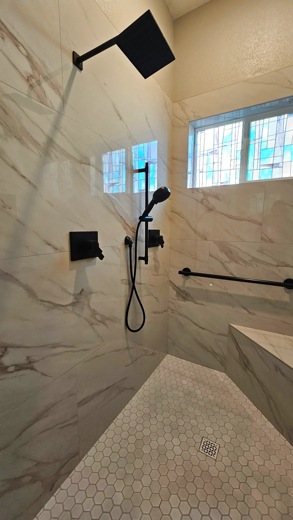 After: close-up of the Roseville shower matte black square rain head, handheld on slide bar, matte black shower controls and Calacatta porcelain walls