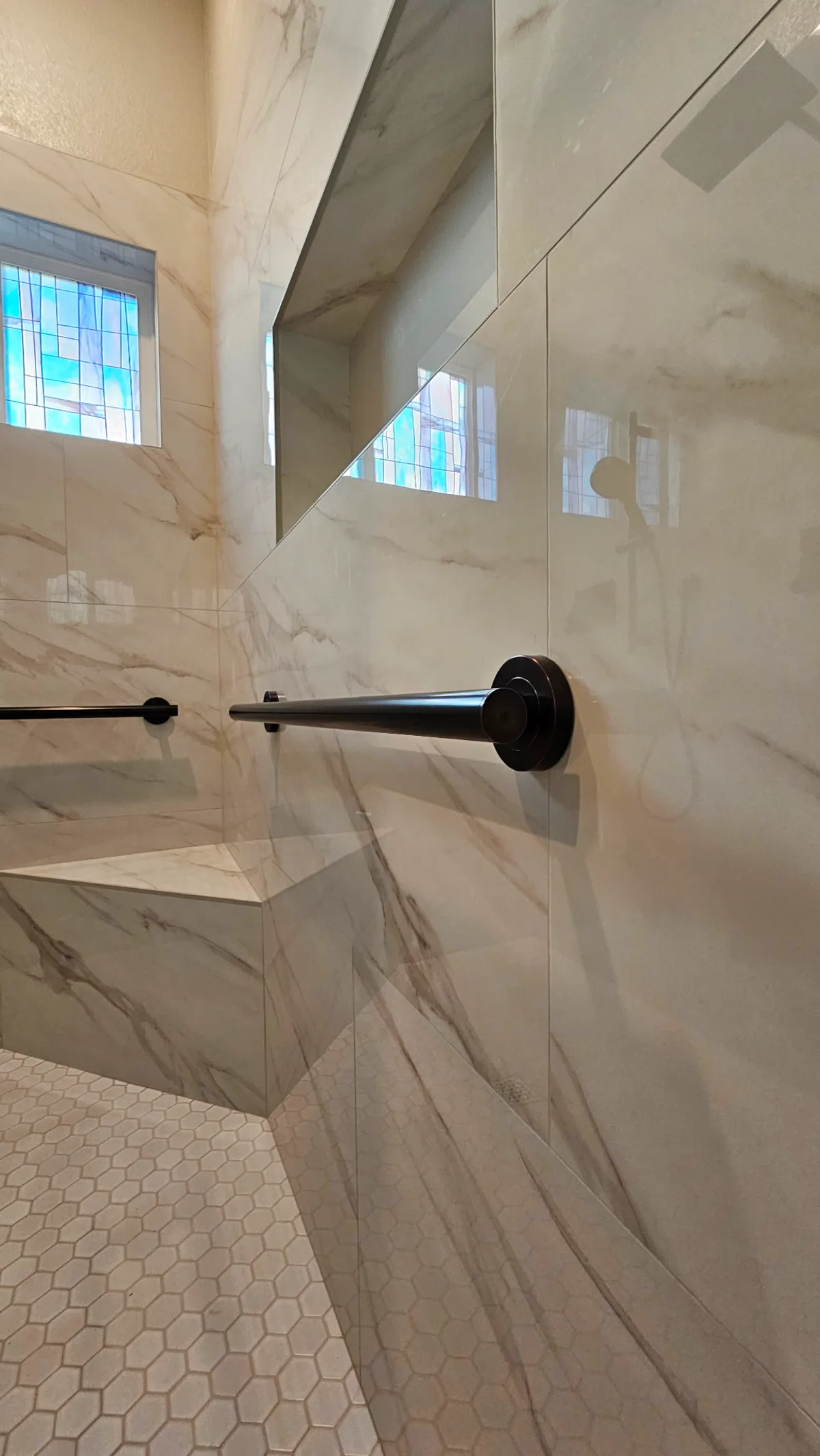 After: Roseville roll-in shower close-up of custom white Calacatta marble corner bench, matte black grab bar and large-format porcelain walls with a frameless glass panel