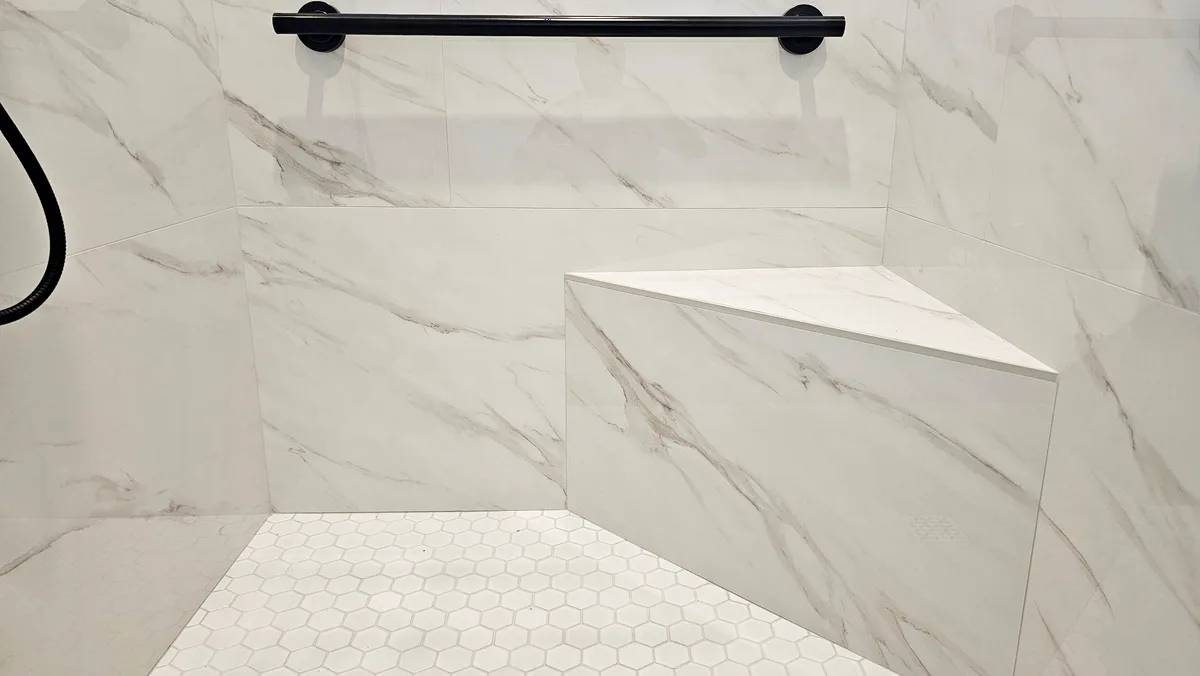 After: Roseville roll-in shower landscape view of two matte black 36-inch grab bars, custom white marble corner bench and white hex mosaic floor