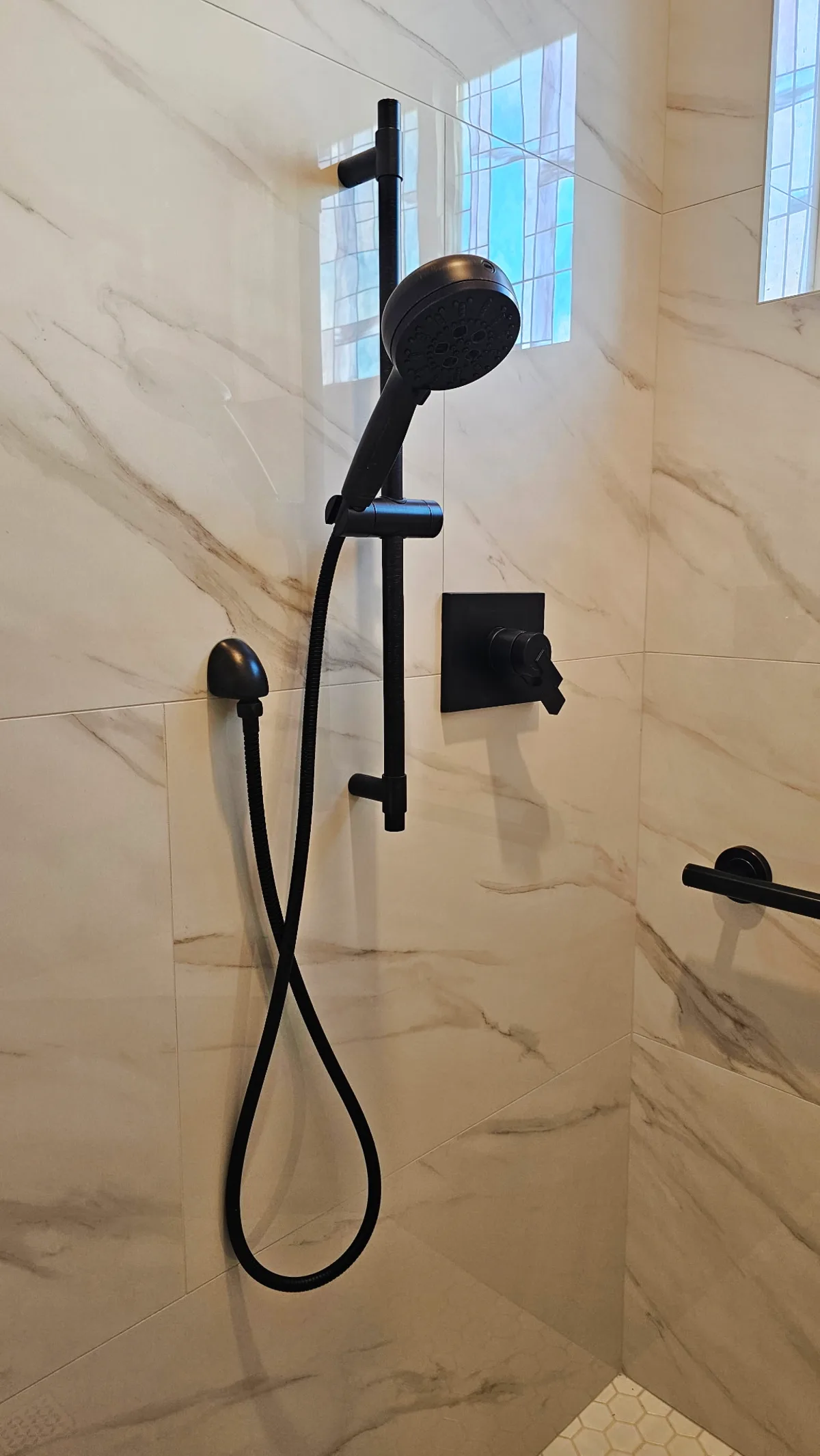 After: Roseville shower handheld on matte black slide bar with matte black shower control, matte black supply elbow and Calacatta marble-look porcelain walls