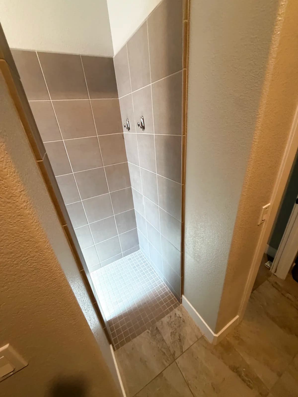 Before: Roseville dated walk-in shower with small square tile walls, mosaic floor and a tiled step at the entry blocking wheelchair access