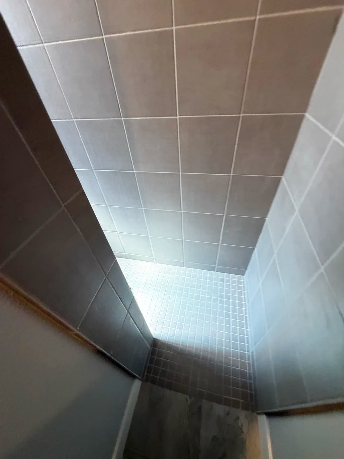 Before: Roseville shower interior with dated tan small tile walls, tile-topped half wall and a built-in tiled bench, viewed from above