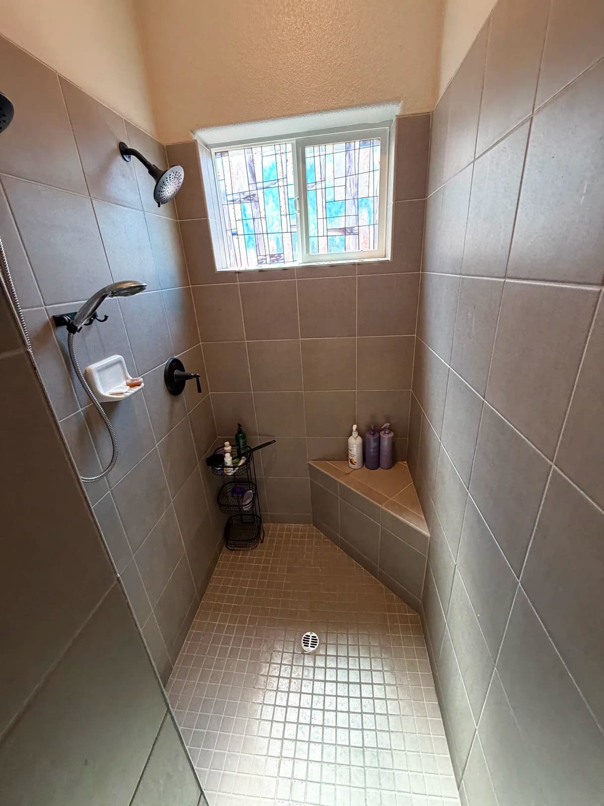 Before: Roseville shower full view with dated small-square tan tile walls, stained-glass privacy window, built-in tile bench and small mosaic shower floor