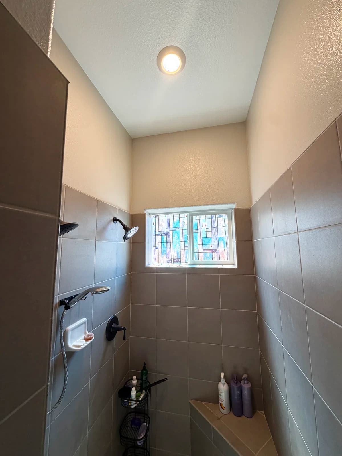 Before: Roseville shower showing the shower head wall, dated square-tile floor and old chrome fixtures