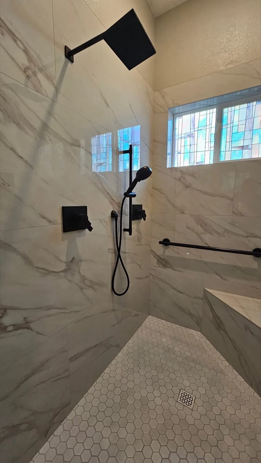 After: Roseville accessible shower showing built-in bench tiled in marble-look porcelain and matte black grab bar on back wall