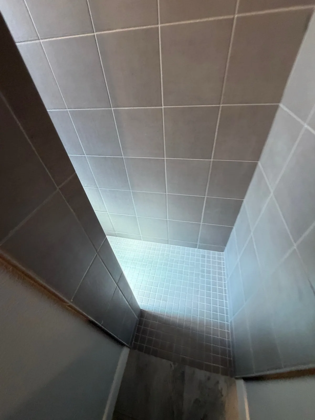 Before: Roseville shower interior showing cramped grey tile stall with small mosaic floor and high curb threshold