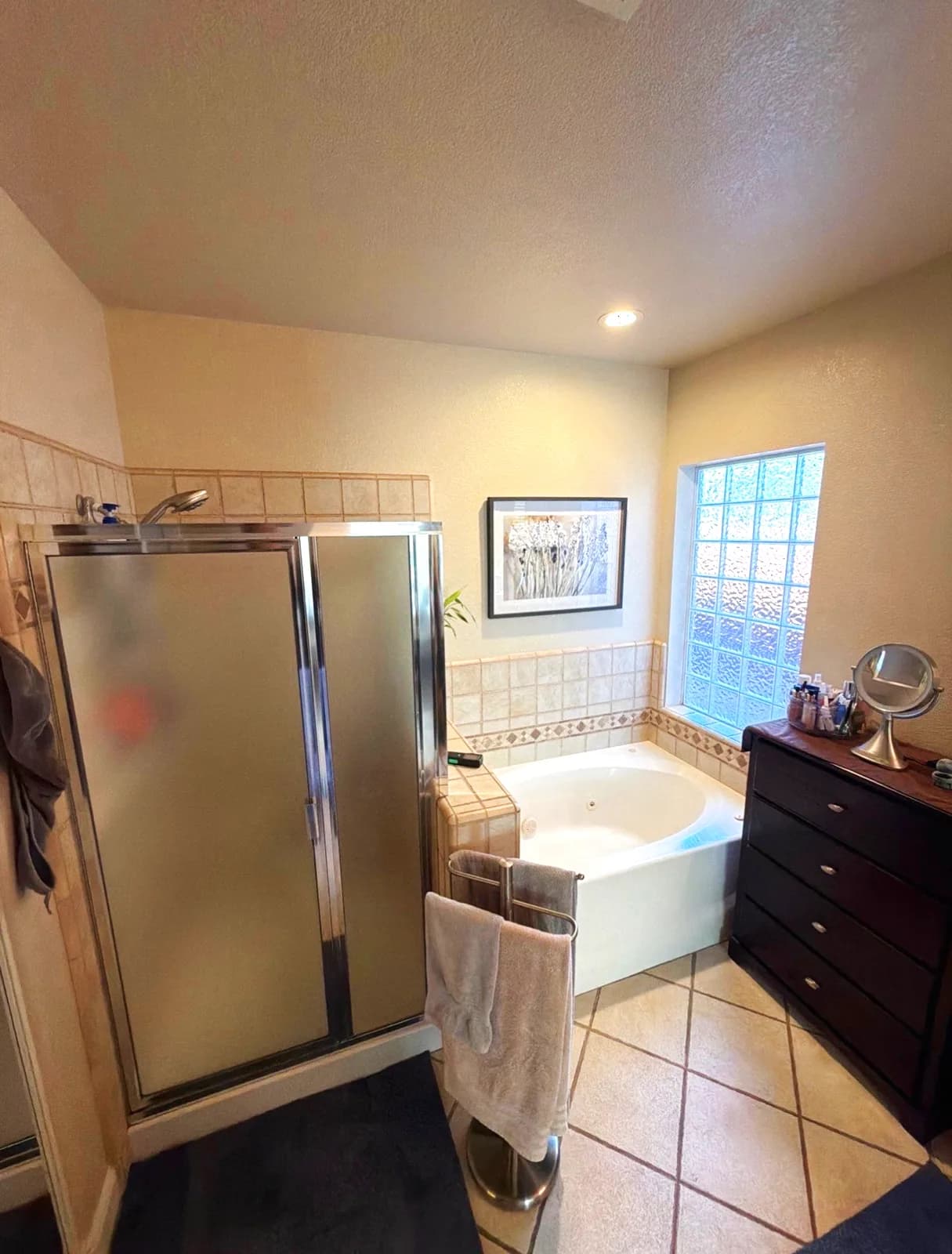 Before: framed shower stall with clouded glass beside the corner tub