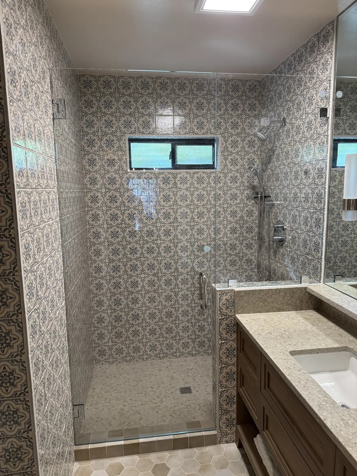 After: Arden hallway bathroom shower with floor-to-ceiling vintage Moroccan-pattern tile and chrome shower valve, viewed through the glass enclosure