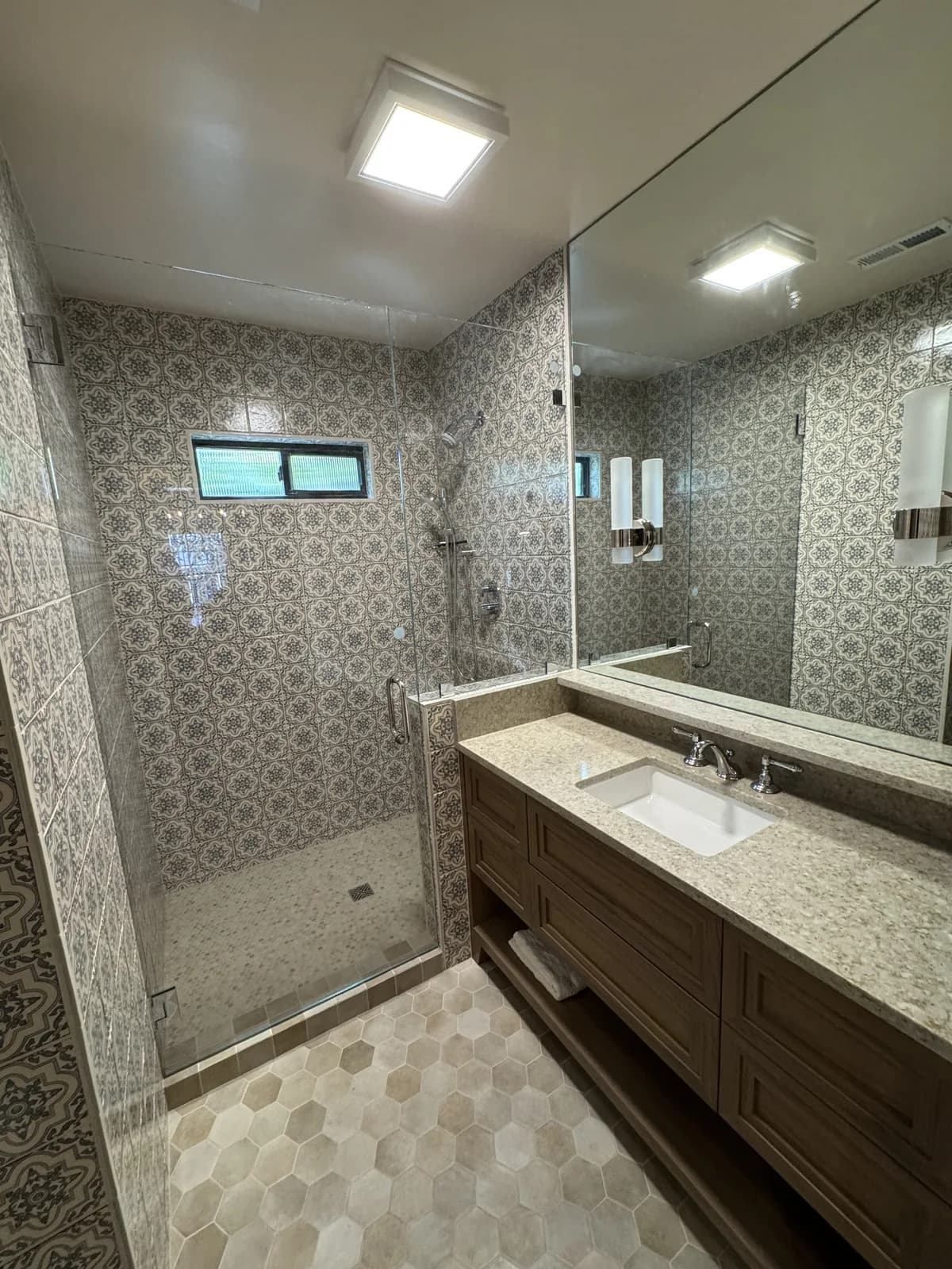 After: Overhead view of the Arden hallway bathroom showing the patterned tile shower, glass door, hex marble floor and custom dark vanity
