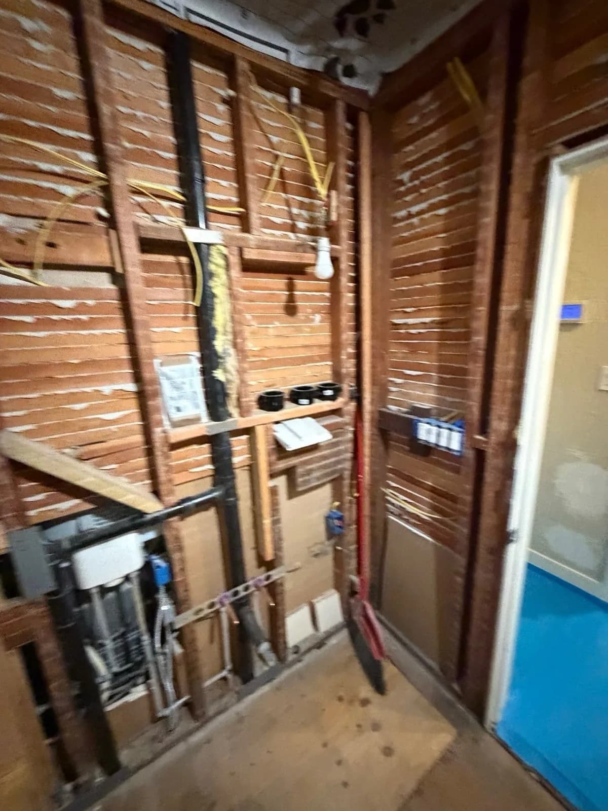 Before: Arden hallway bathroom with no drywall — exposed studs, wiring and plumbing near the door entry
