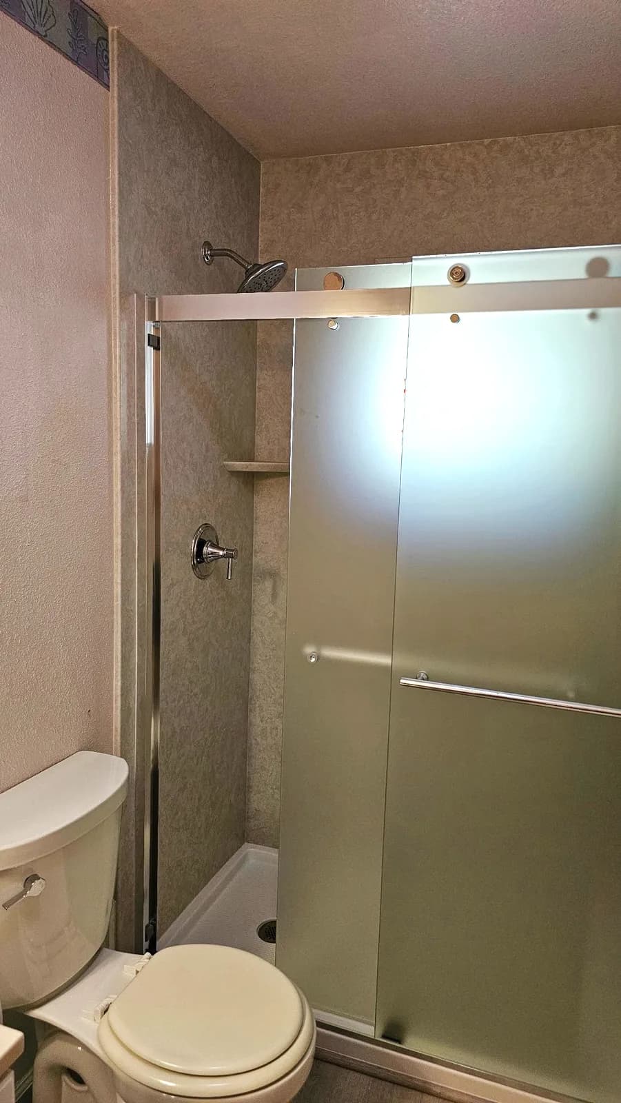 After: frosted sliding glass door and marble-look acrylic walls beside the toilet in an Auburn bathroom