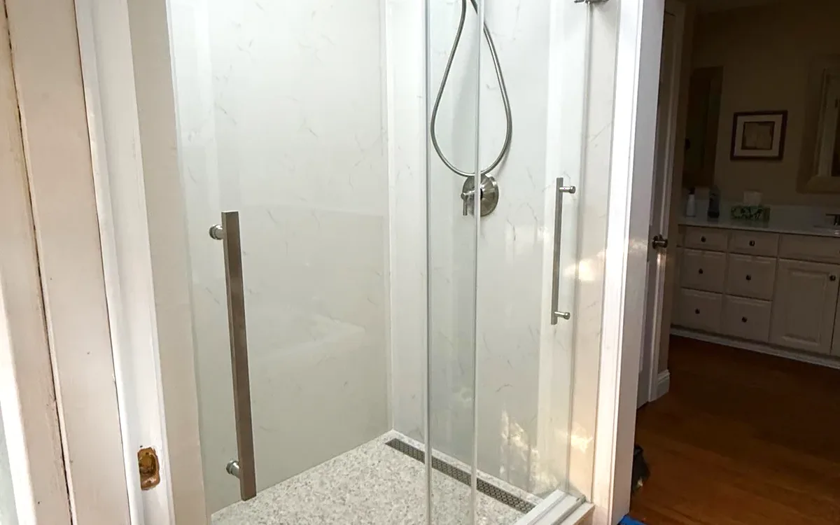 Frameless sliding glass door on a top-mounted track with stone-look floor and linear drain