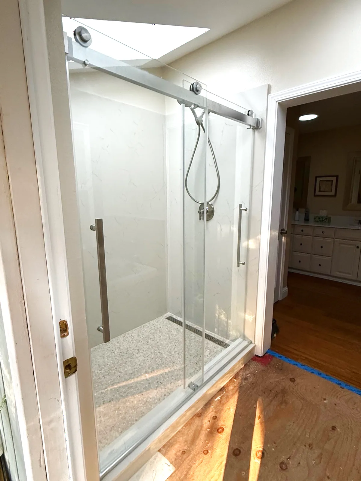 After: frameless sliding glass door on a top-mounted track with stone-look floor and linear drain