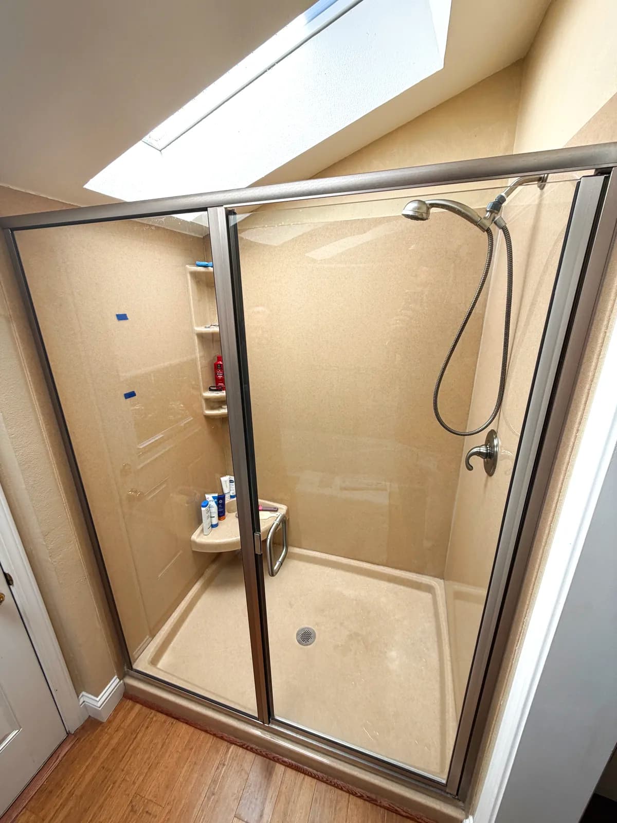 Before: yellowed one-piece fiberglass shower with framed sliding doors under a skylight in Auburn, CA