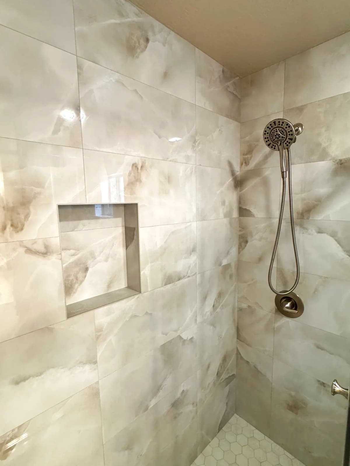 After: brushed nickel handheld shower on marble-look porcelain tile