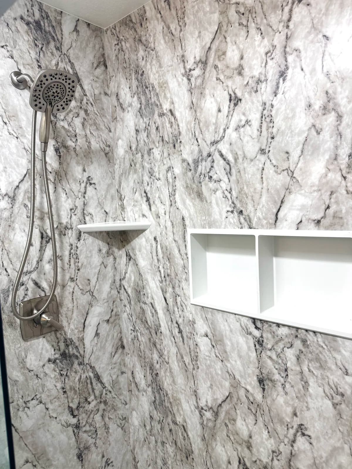 After: chrome handheld shower on a slide bar beside a twin niche and corner shelf on marble-look acrylic walls