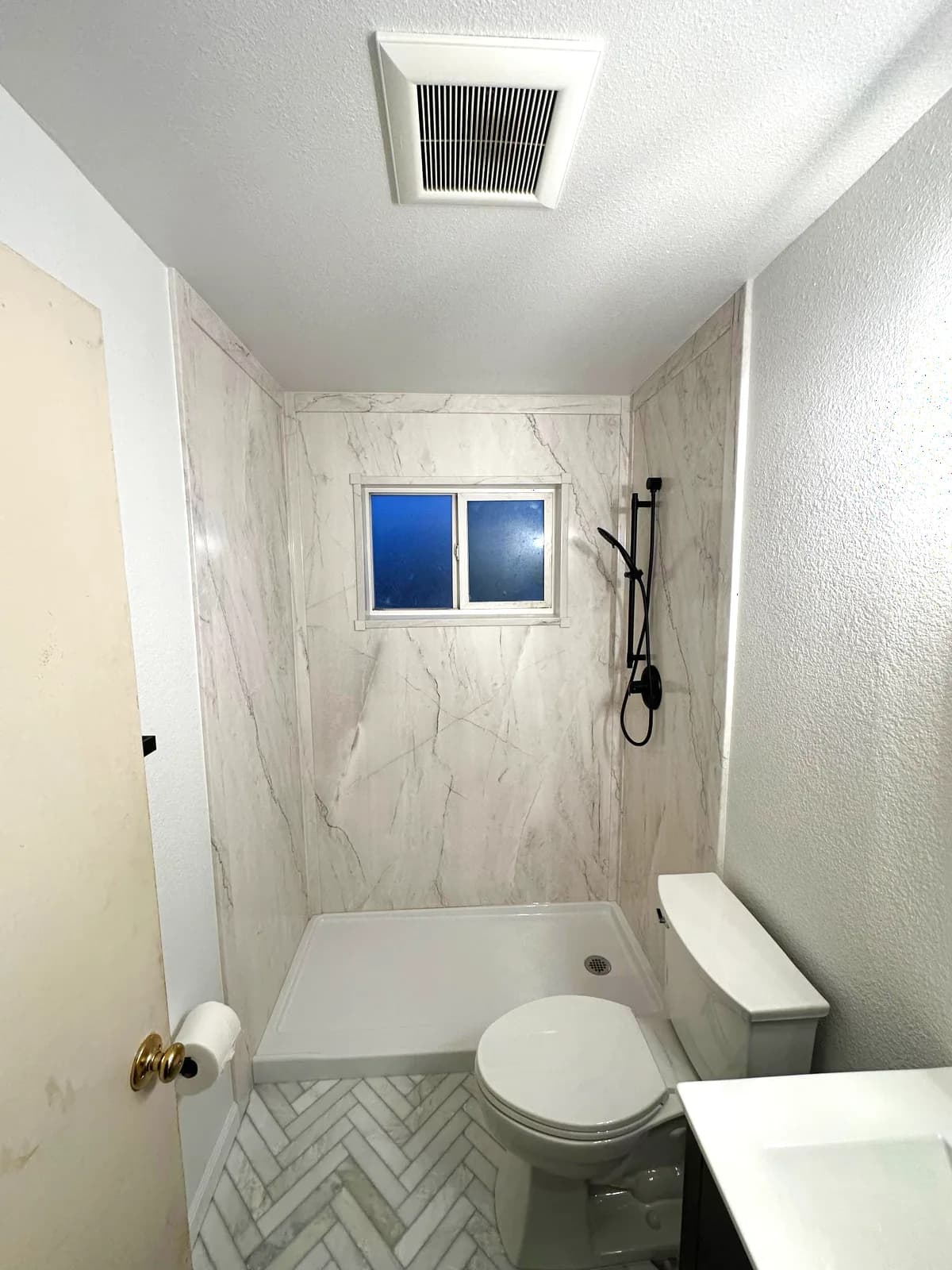 After: Citrus Heights bathroom with black shaker vanity, round mirror, herringbone floor and acrylic-walled shower