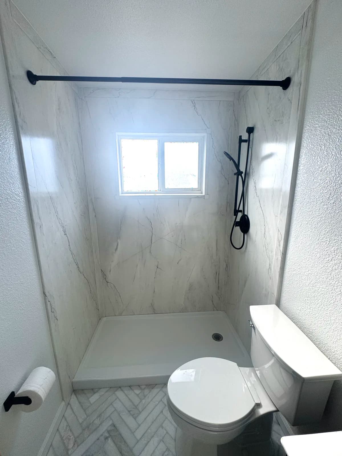 After: marble-look acrylic wall panels and matte black shower trim