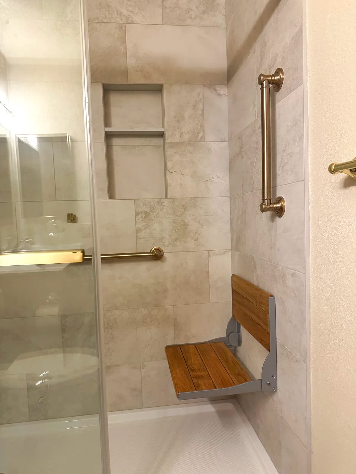 After: fold-down teak seat and brushed gold grab bar inside the shower