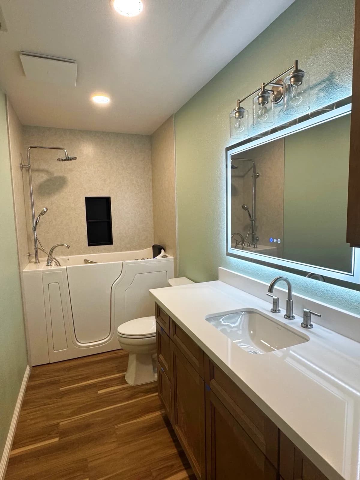 After: full view of the Roseville bathroom with the walk-in therapy tub on the left and the warm-wood vanity with backlit LED mirror on the right