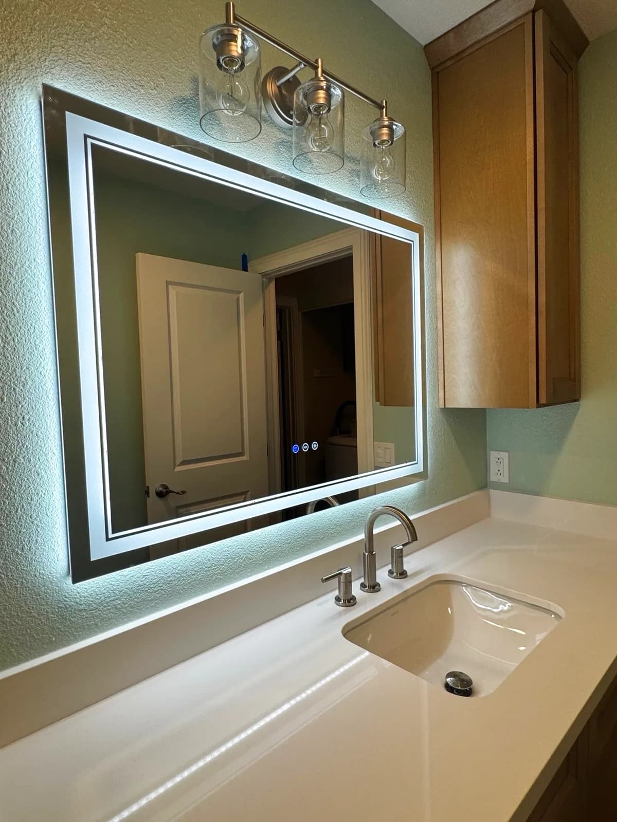 After: close-up of the Roseville bathroom backlit LED mirror, 3-globe brushed nickel vanity light fixture and white quartz countertop
