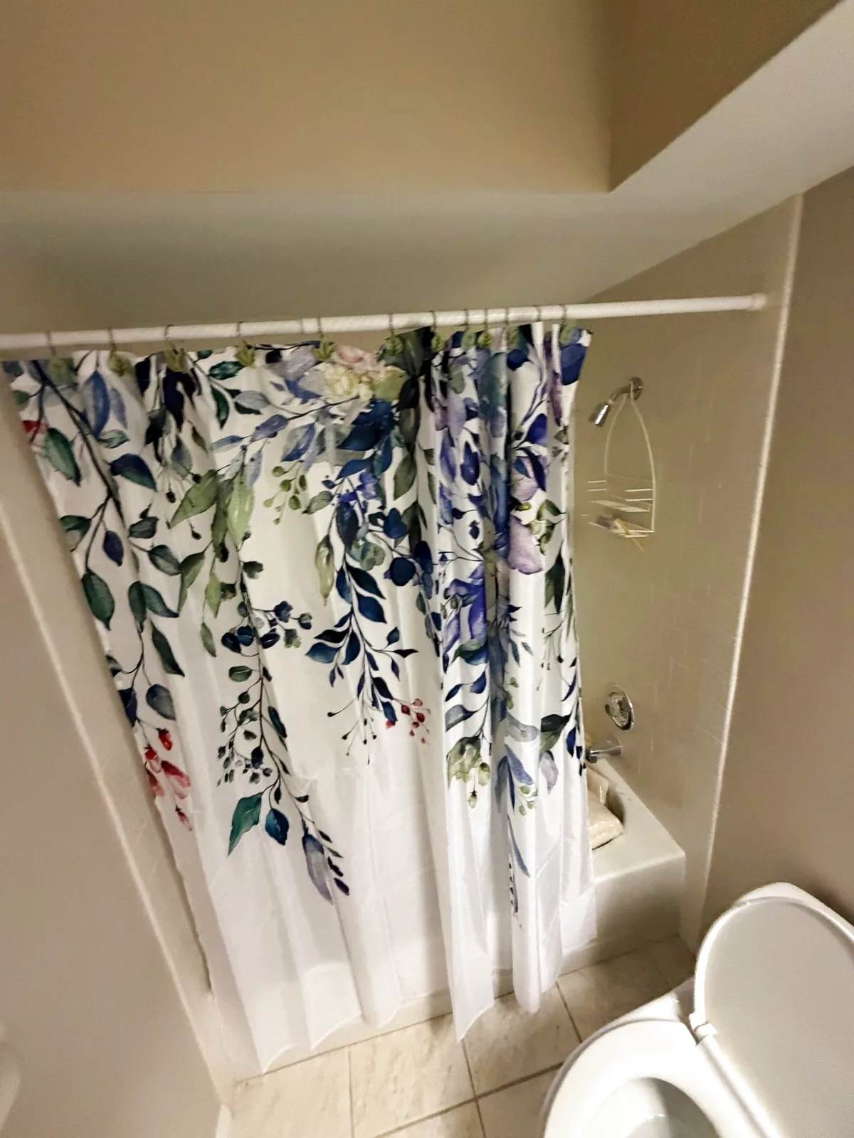 Before: Roseville alcove tub behind a floral shower curtain with dated white tile walls and a small floor tile