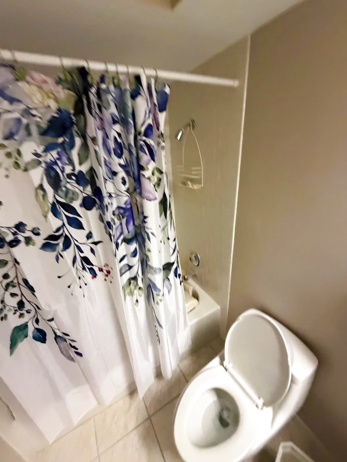 Before: Roseville alcove tub with pulled-back floral curtain showing dated white tile surround, chrome bath spout and a wire shower caddy