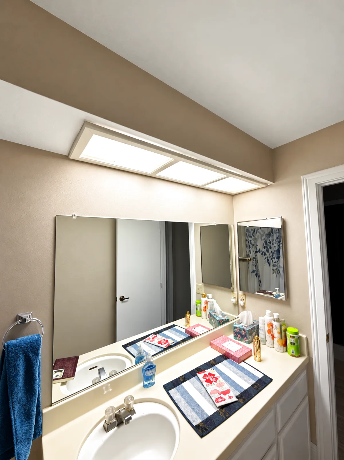 Before: Roseville bathroom vanity with a boxed fluorescent light soffit over a plain frameless mirror and tan walls