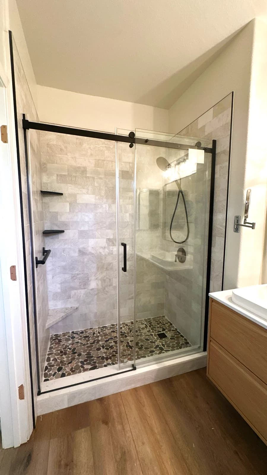 After: walk-in shower with marble-look porcelain, pebble floor, black-framed sliding door and floating vanity in Natomas