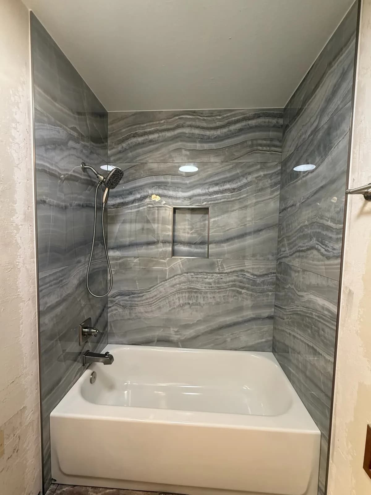 After: new white alcove tub with floor-to-ceiling grey onyx-look porcelain tile walls, recessed niche and handheld shower in Woodland, CA