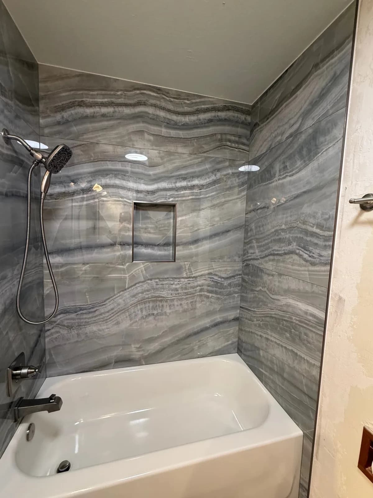 After: brushed nickel handheld shower head on a slide bar and matching tub spout against grey veined porcelain tile