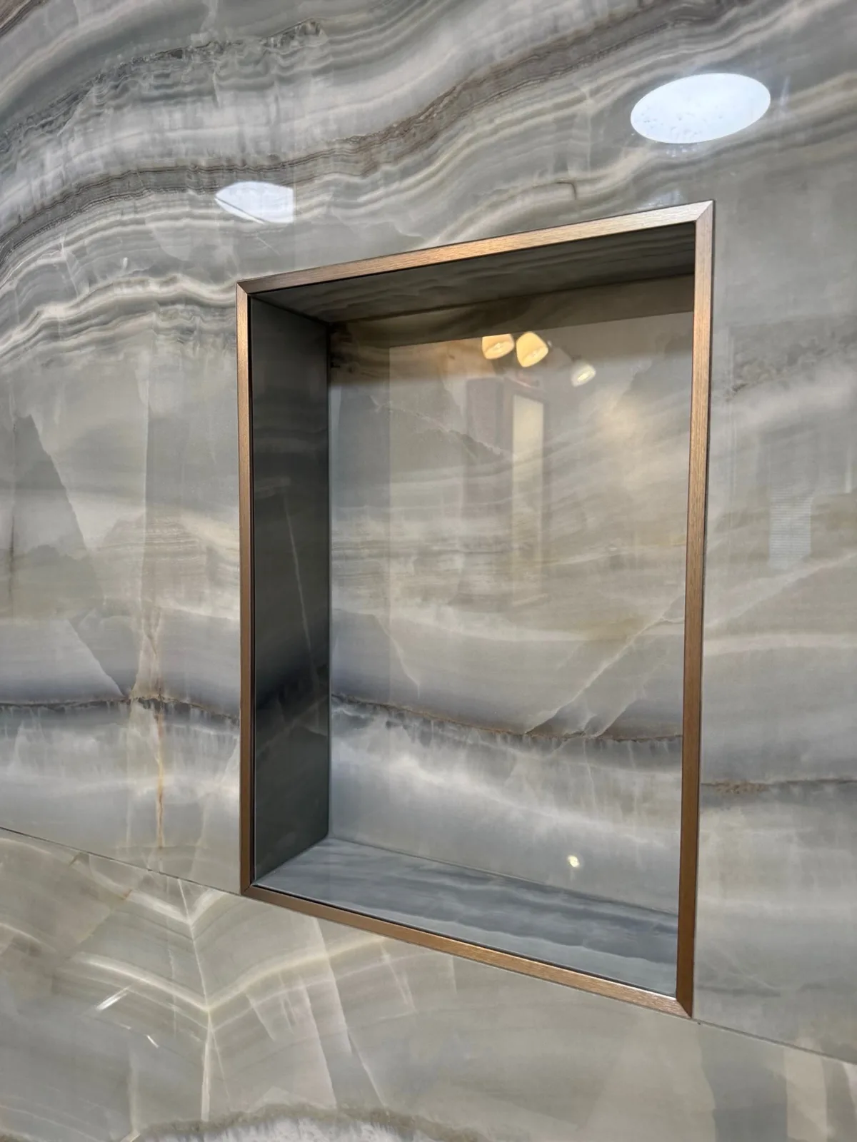 After: close-up of the recessed shower niche with bronze metal edge trim set into onyx-look porcelain tile